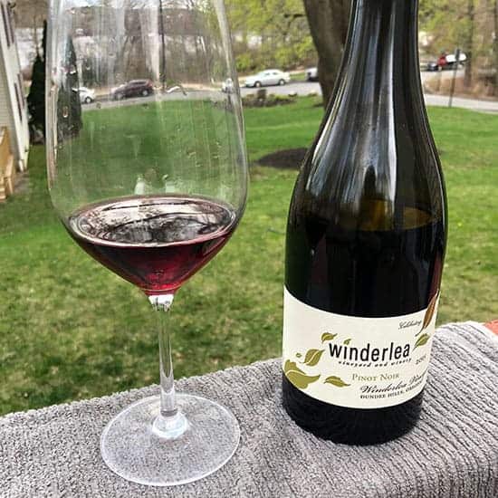 bottle of Winderlea Pinot Noir outside on a deck, with a glass of red wine poured next to it.