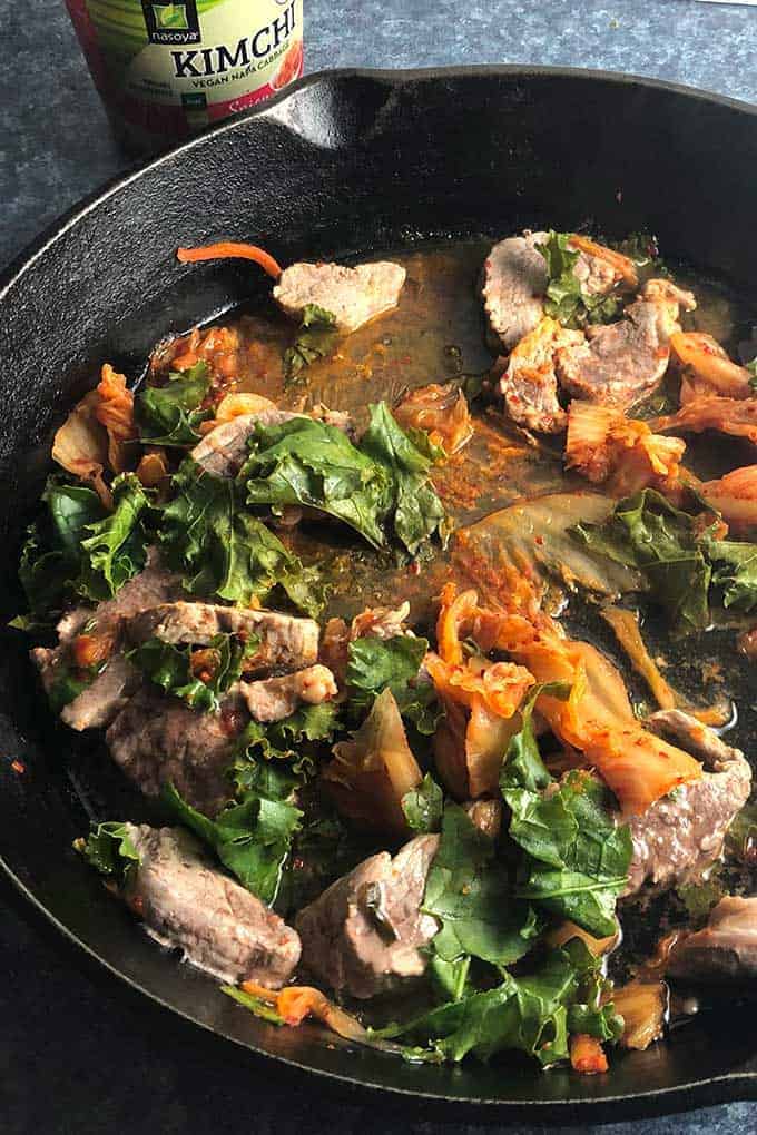 pork tenderloin cooking in skillet with kimchi and kale.