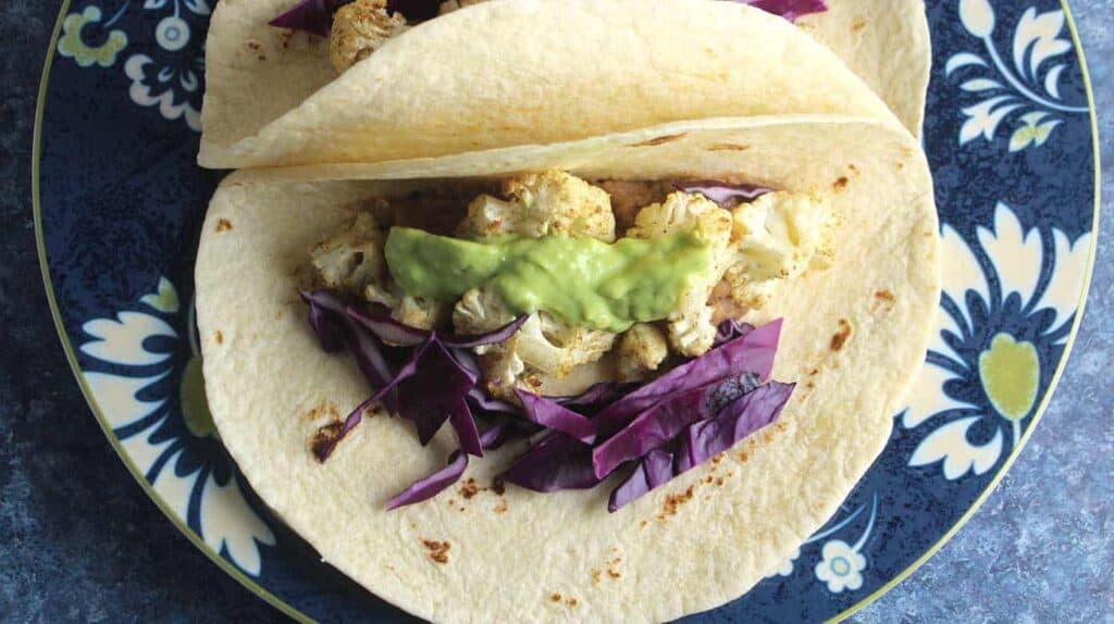 white soft tacos with roasted cauliflower, red cabbage and avocado cream.