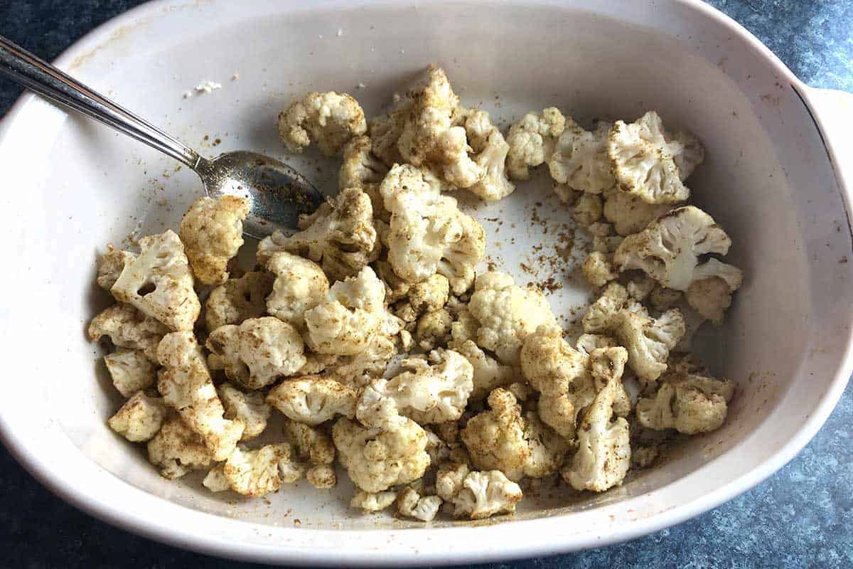 preparing to roast cauliflower in a white baking dish.