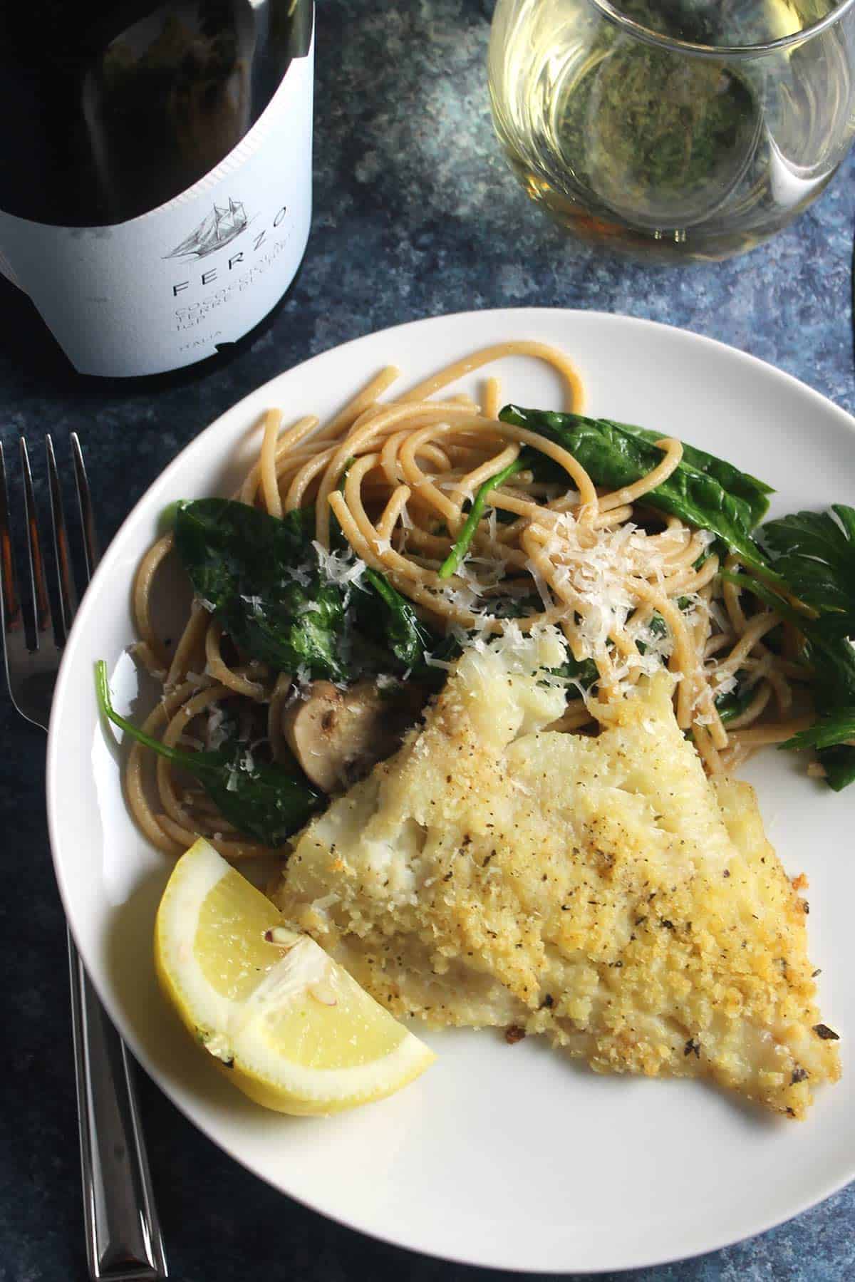 a plate of baked haddock with pasta along with glass of white wine.