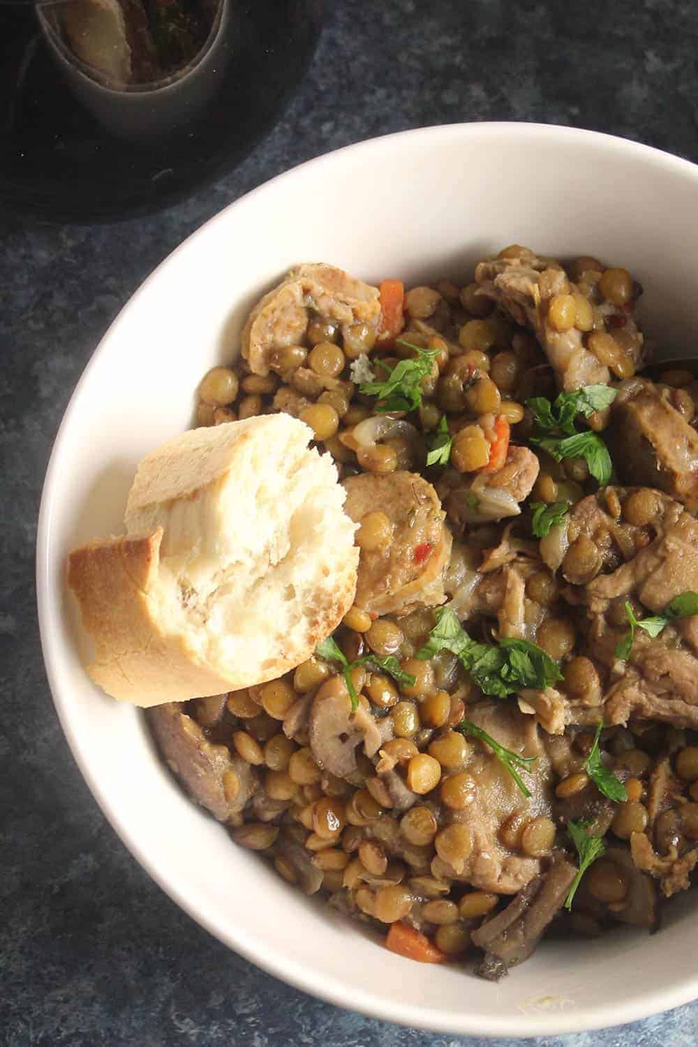 bowl of chicken lentil stew with a piece of French bread on the side.