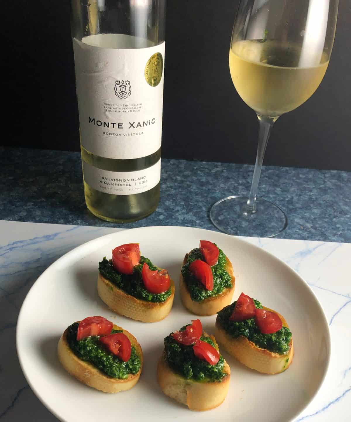 crostini topped with pesto and tomatoes, served with a white wine