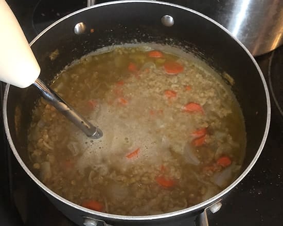 pureeing lentil soup with a handheld blender.