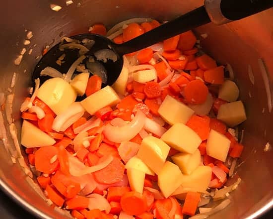 adding potatoes to carrot soup.