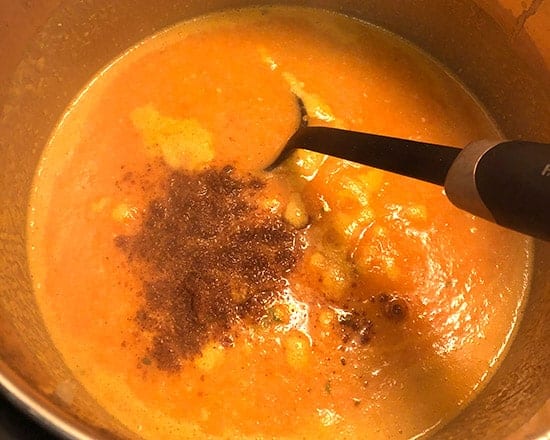 adding spices to carrot ginger soup.