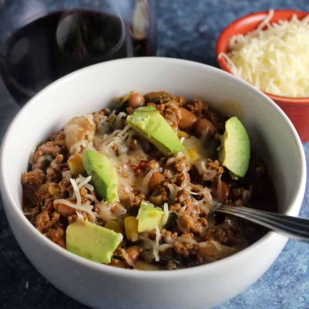 bowl of ground beef chili topped with avocado and cheese.