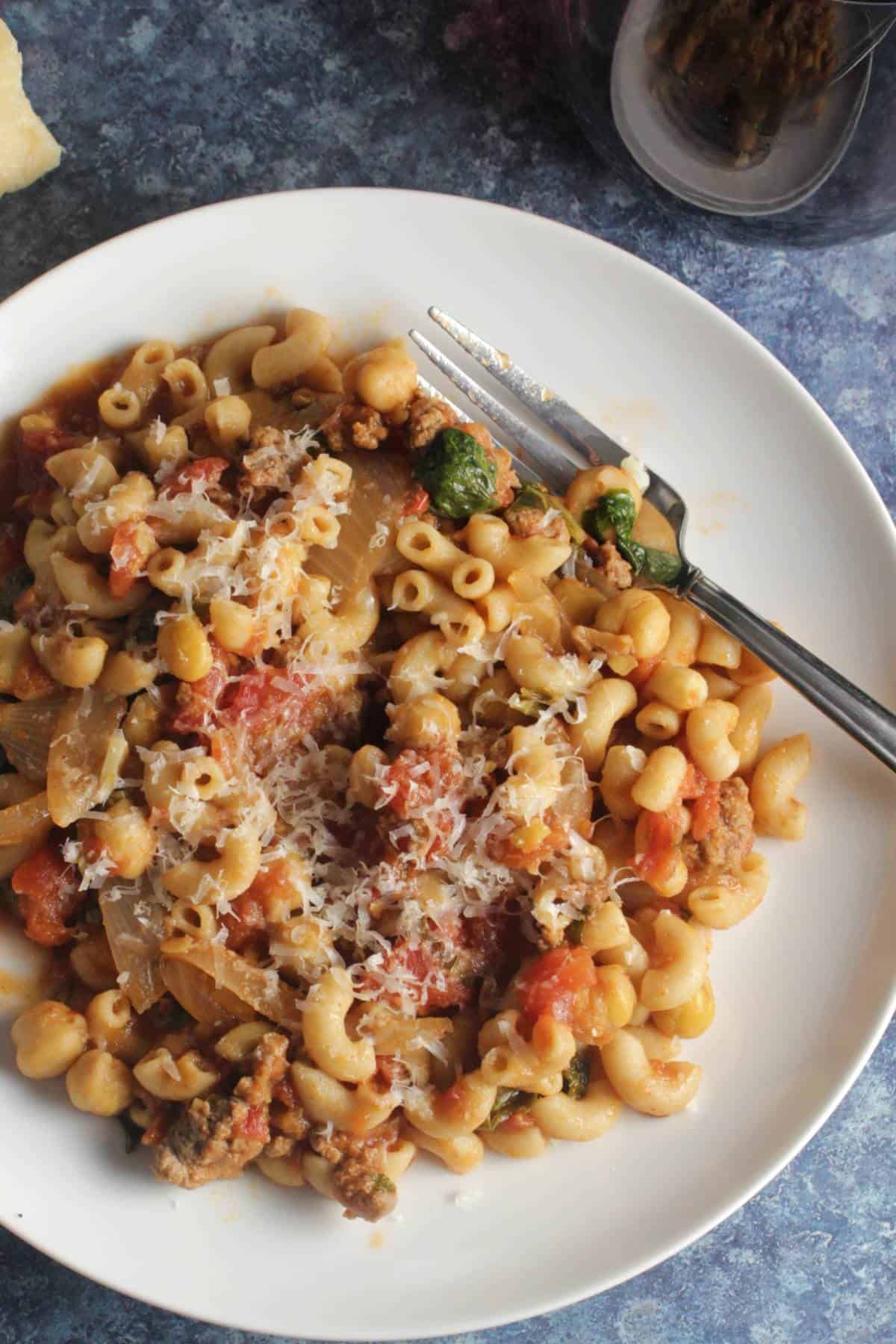 elbow macaroni tossed with a ground beef and chickpea tomato sauce, served on a white plate.