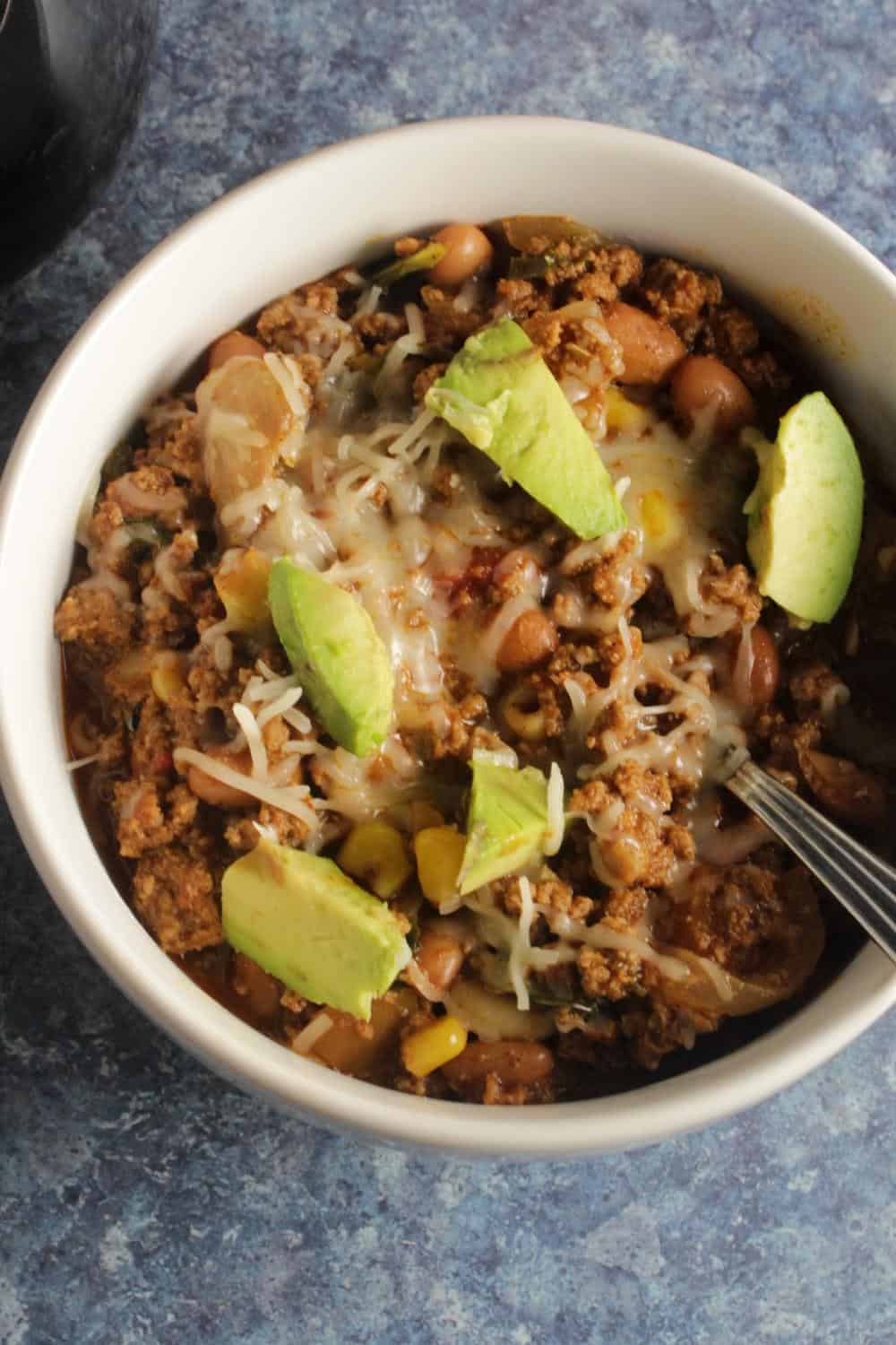 bowl of beef chili topped with avocado and cheese.