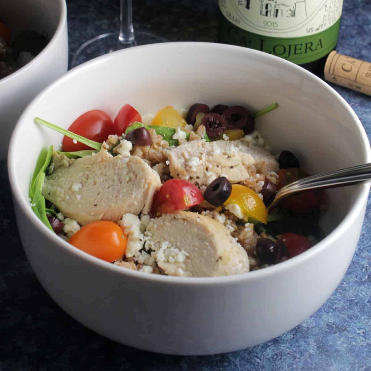 bowl with salad greens topped with chicken, tomatoes and olives.