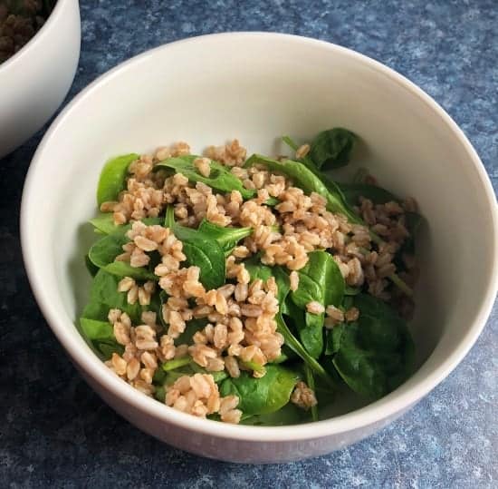 baby spinach topped with farro in a white bowl.