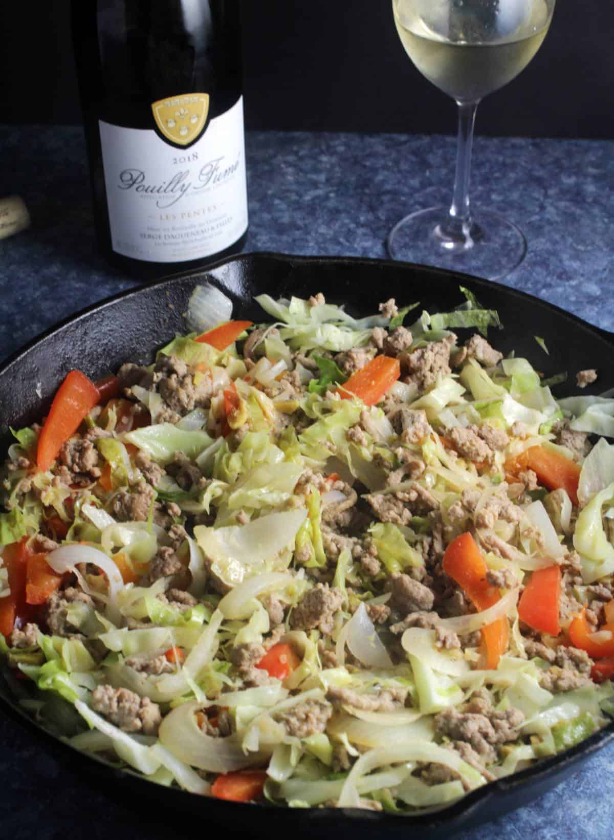 turkey and cabbage in skillet with bottle of wine.