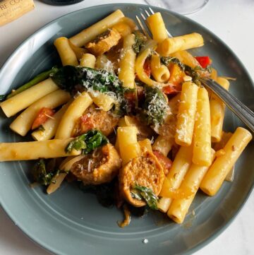 ziti tossed with a veggie pasta sauce with greens, served on a gray plate.