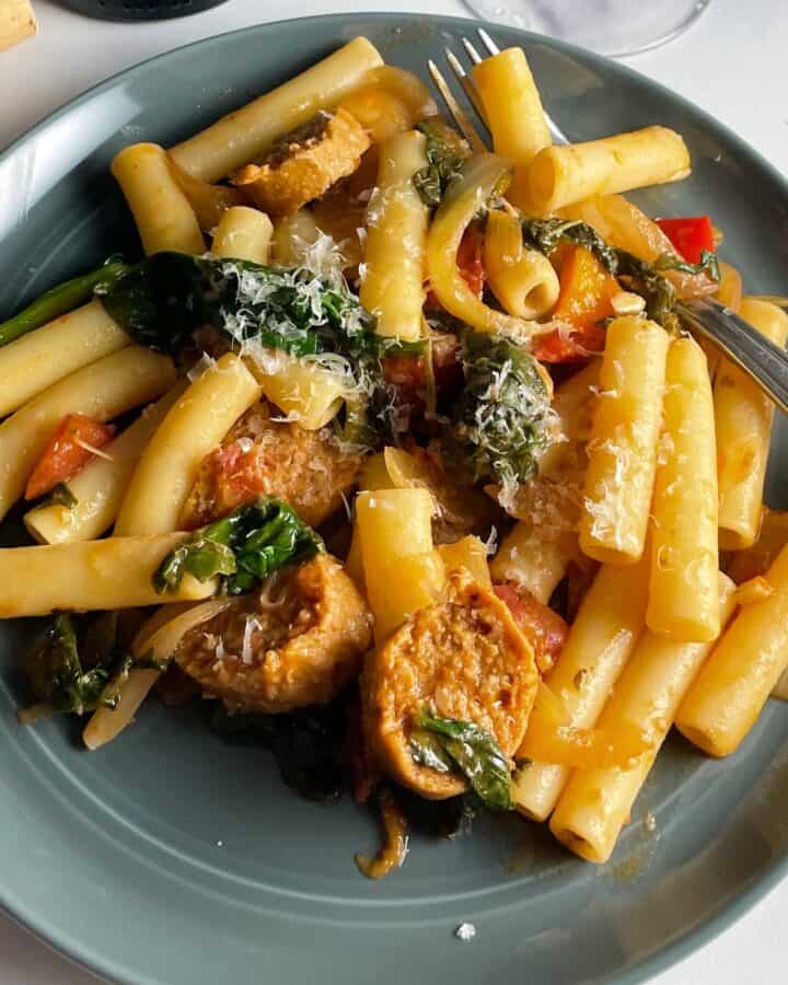 ziti tossed with a veggie pasta sauce with greens, served on a gray plate.