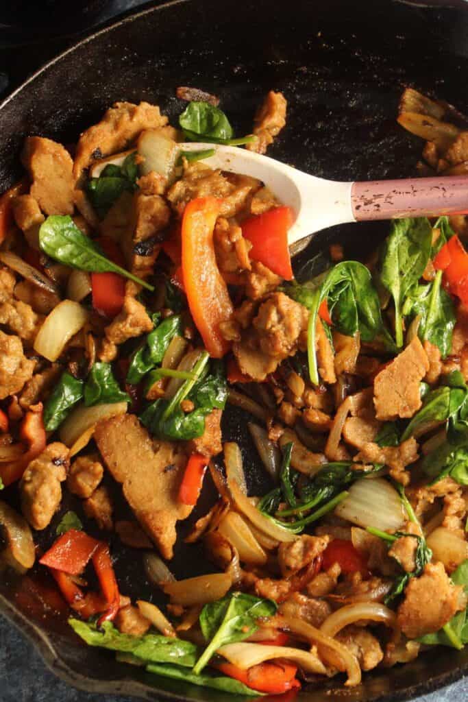 seitan with onions and peppers in a black skillet.