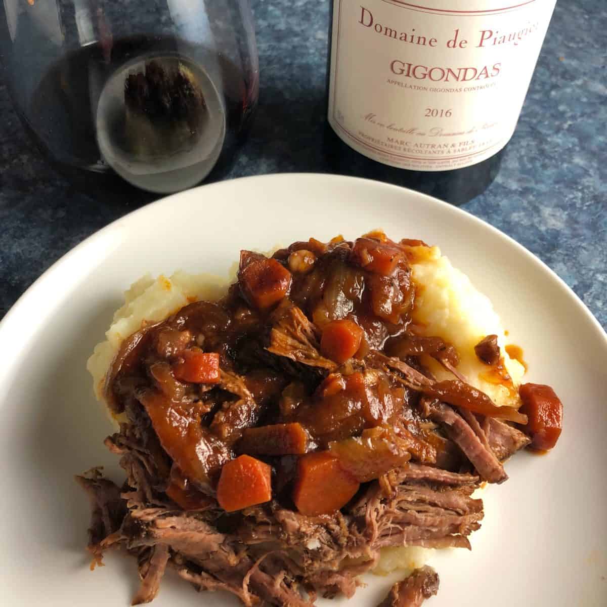 beef brisket served over mashed potatoes, along with a red wine.