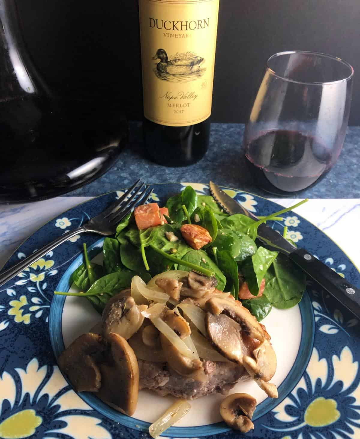 plate with pork chops topped with mushrooms, served with a salad and red wine.