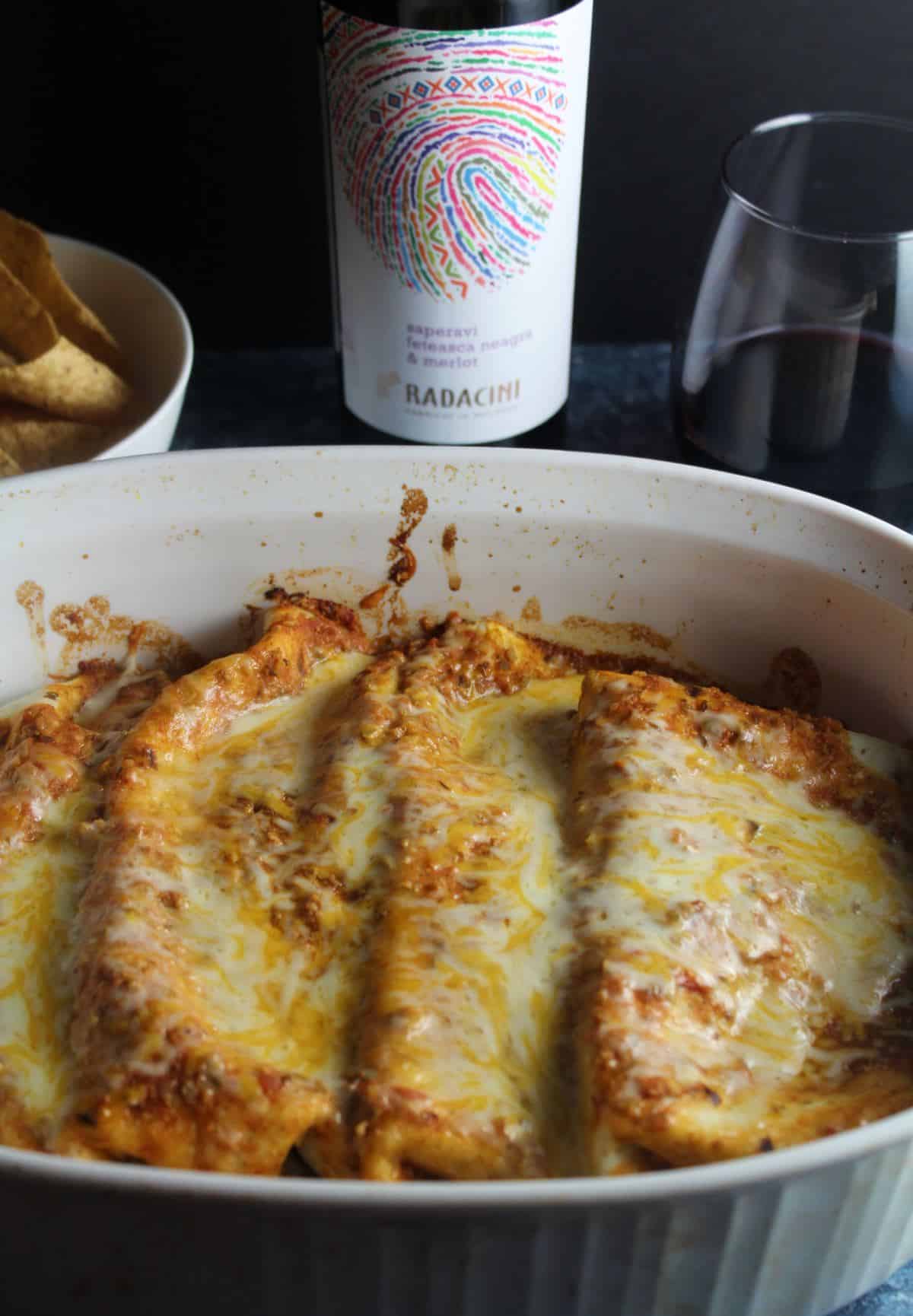 beef and bean enchiladas in a baking dish served with a red wine.