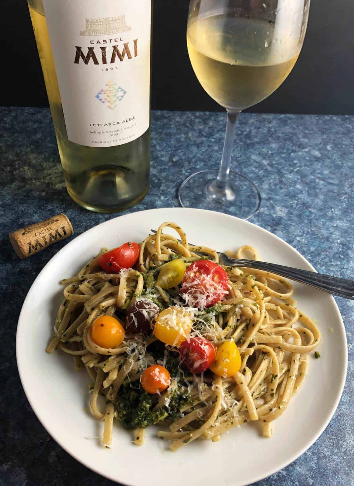 pasta with pesto topped with tomatoes served with a white wine.