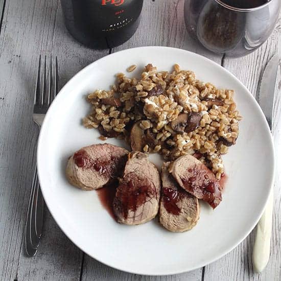 pork tenderloin served with a blackberry Merlot sauce and farro grain, along with a glass of Merlot red wine.