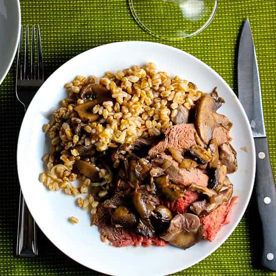 spoon roast with mushrooms and farro on a white plate.