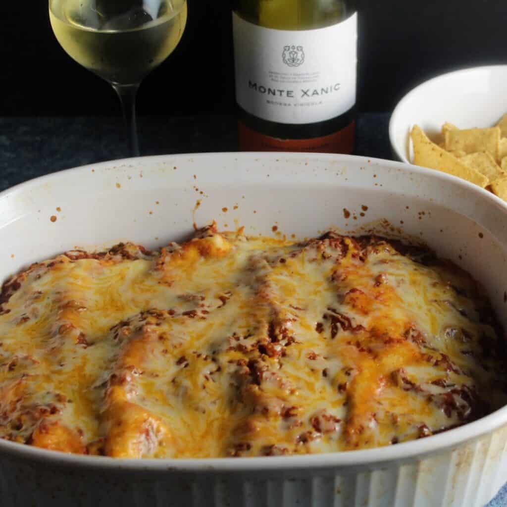 turkey enchiladas in a baking dish with white wine in the background