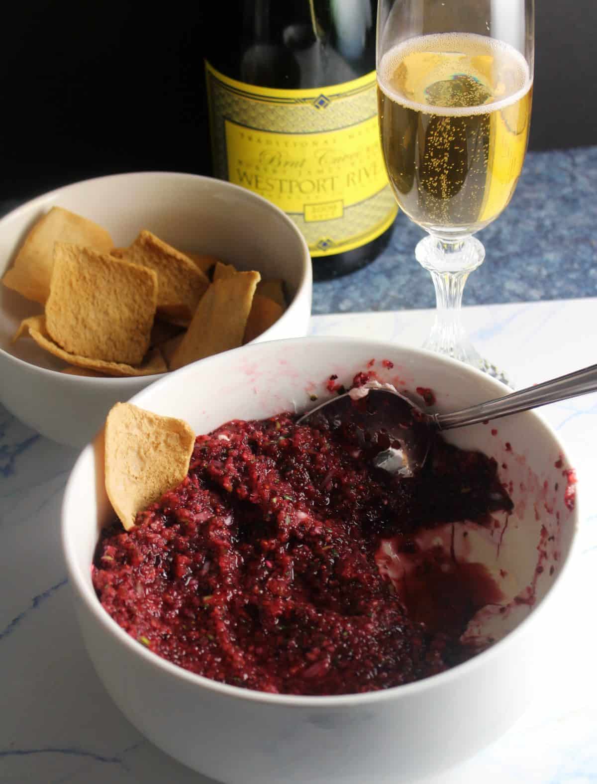 bowl of cranberry jalapeño dip with cream cheese, served with pita chips and sparkling wine.