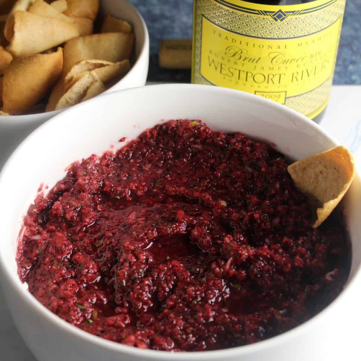 cranberry jalapeno dip in a white bowl served with sparkling wine.