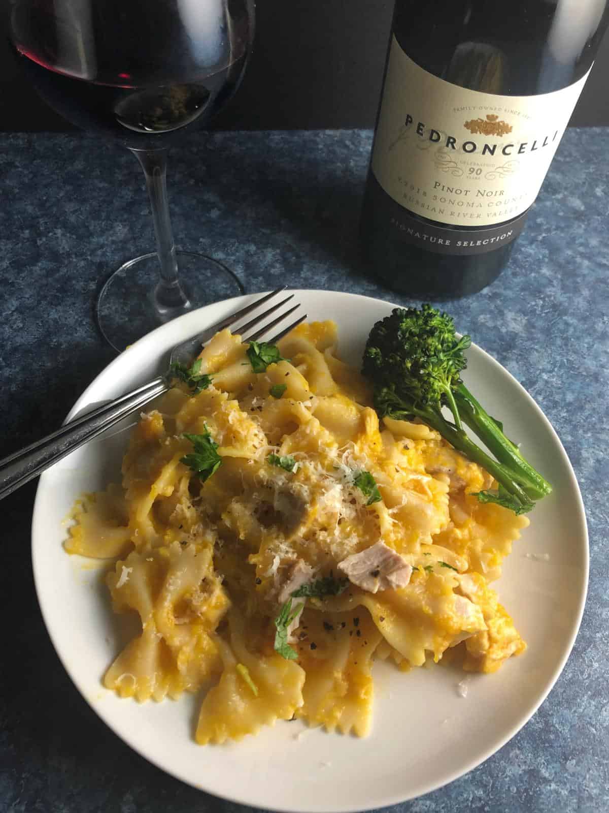 leftover butternut squash pasta on a white plate, served with a glass of red wine.