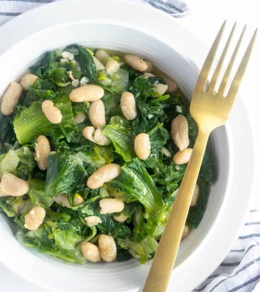escarole and white beans in a white bowl with a fork. image from Pina Bresciani.