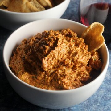 roasted red pepper dip in a white bowl served with pita chips.