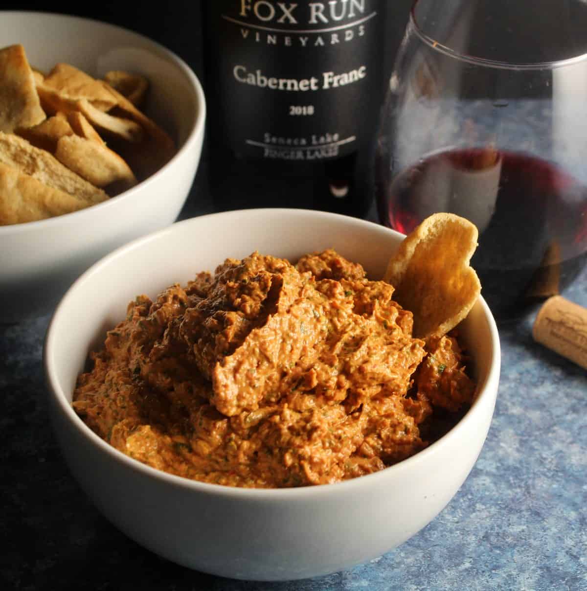 bowl of roasted red pepper dip served with a red wine and pita chips.
