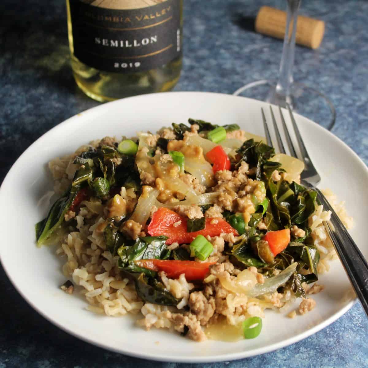 ground pork stir-fry with collard greens served over rice on a white plate.