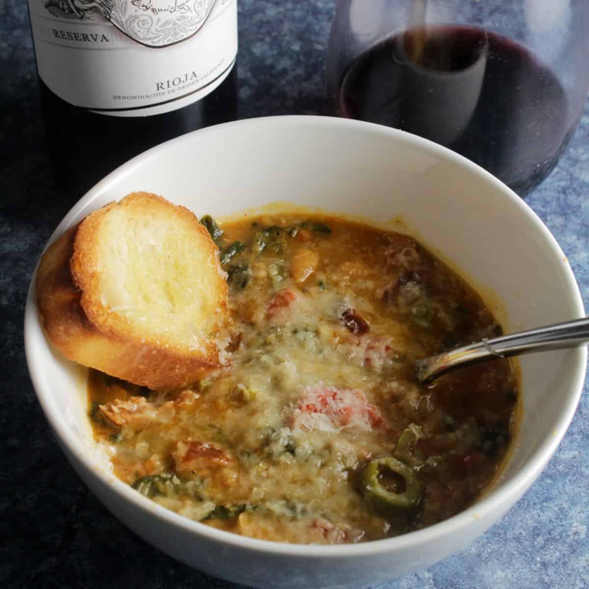 bowl of Spanish white bean stew topped with Manchego cheese, in a white bowl.