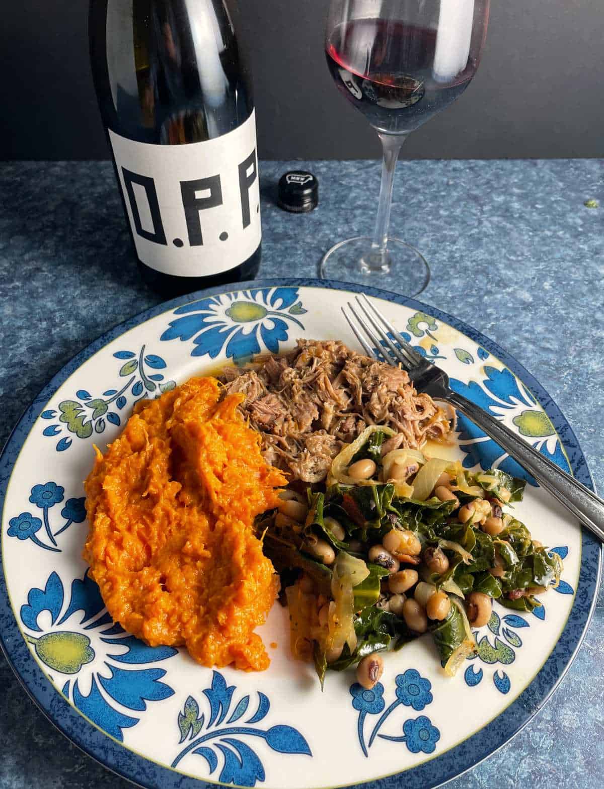 a plate with collard greens and black-eyed peas, pulled pork and sweet potatoes. Served with Pinot Noir wine.