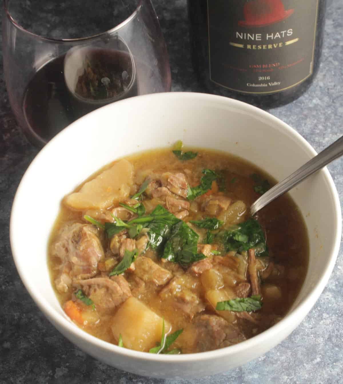 Irish Lamb Stew served in a white bowl along with a red wine.
