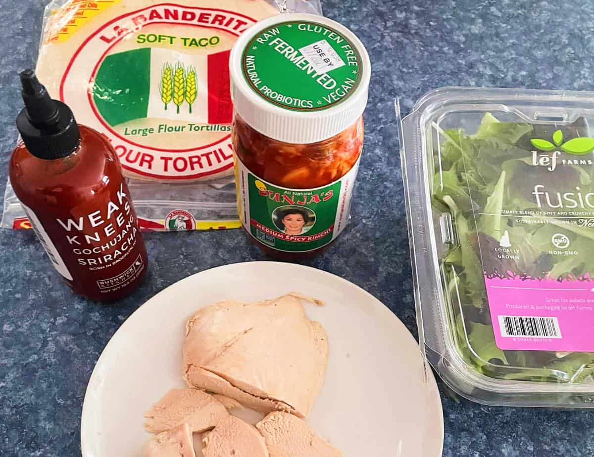 ingredients for Korean chicken wraps assembled- gochujang sriracha, wraps, kimchi, greens and chicken.