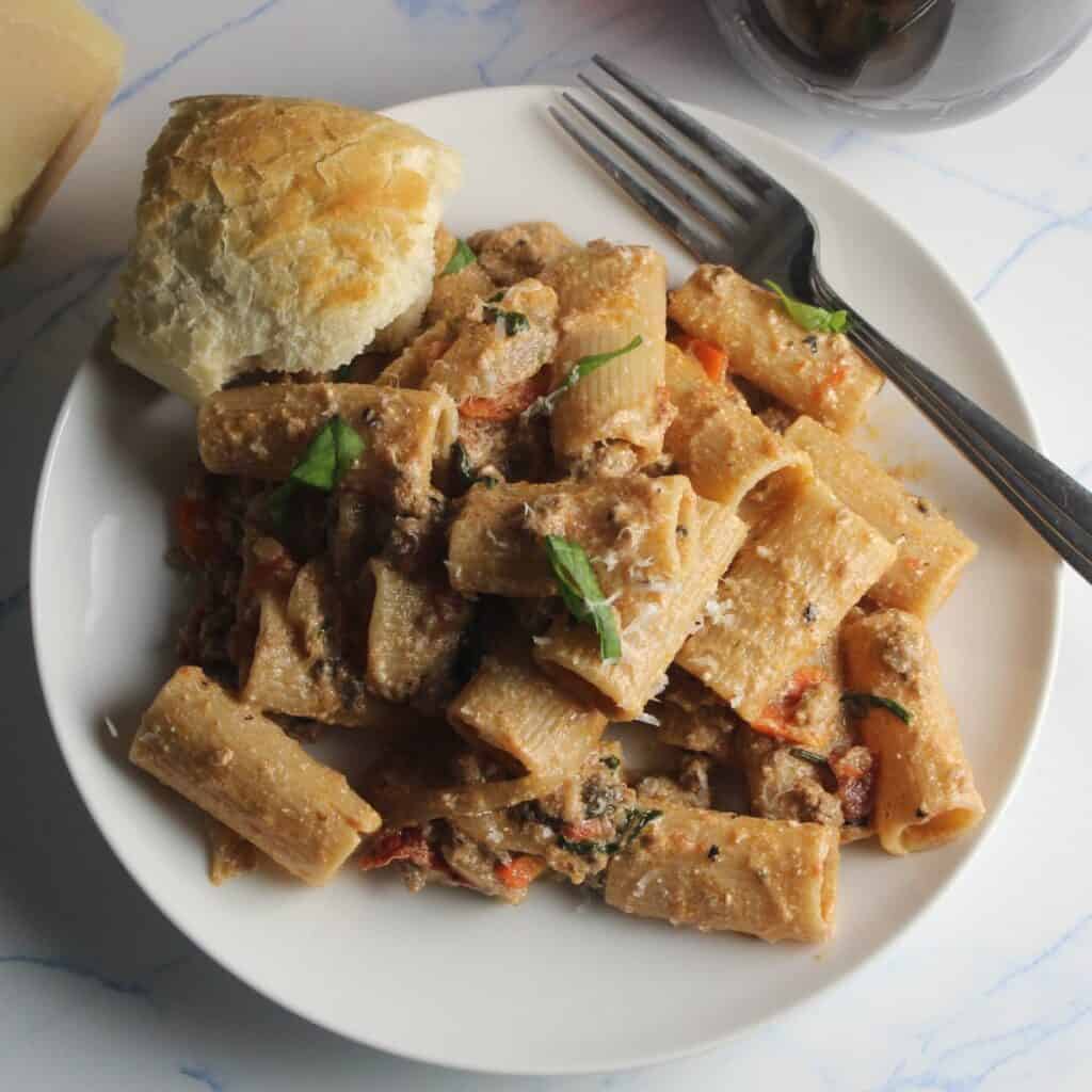 lamb ragu pasta served on a white plate with a piece of bread on the side.