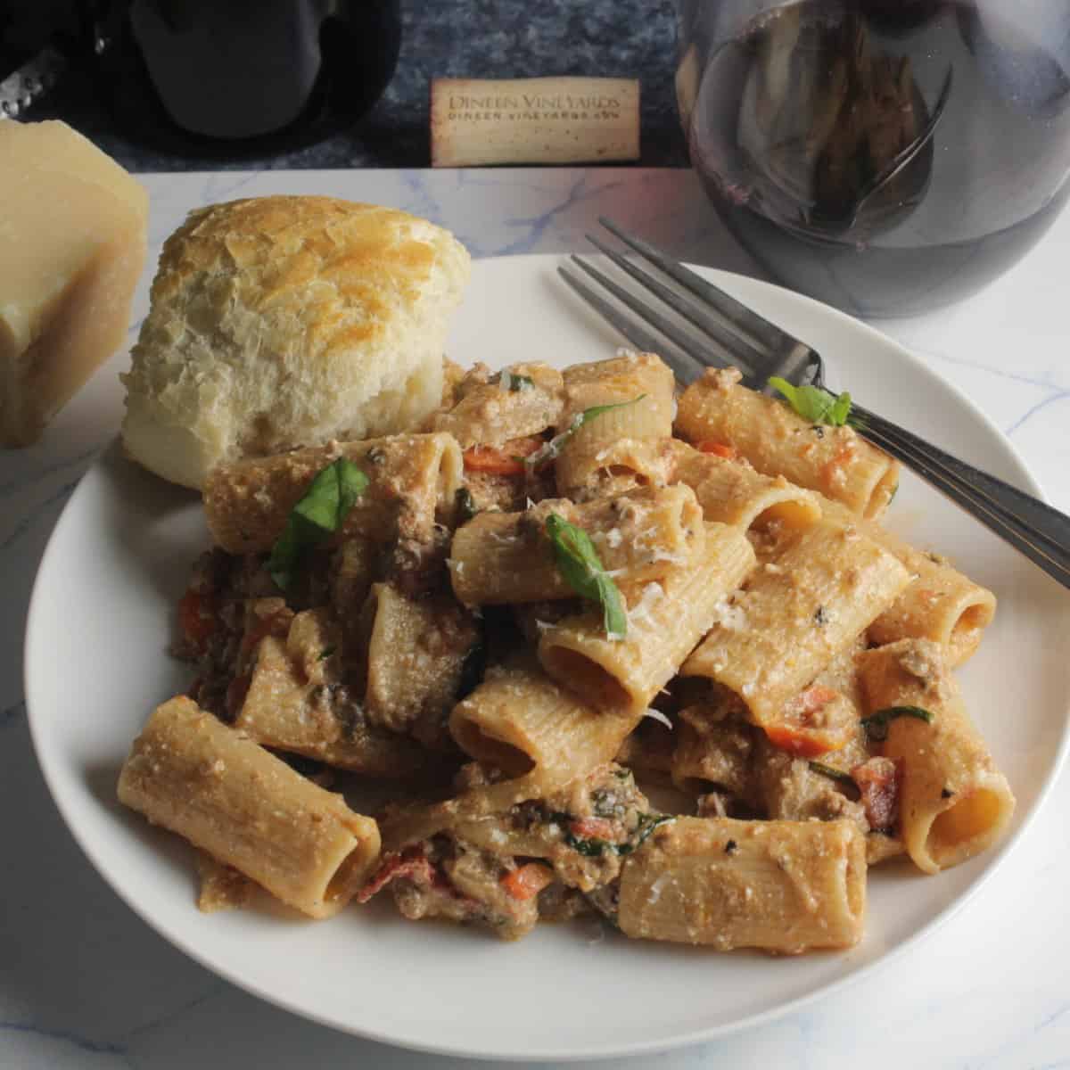 rigatoni pasta with a ground lamb ragu sauce on a white plate, with a side of bread.