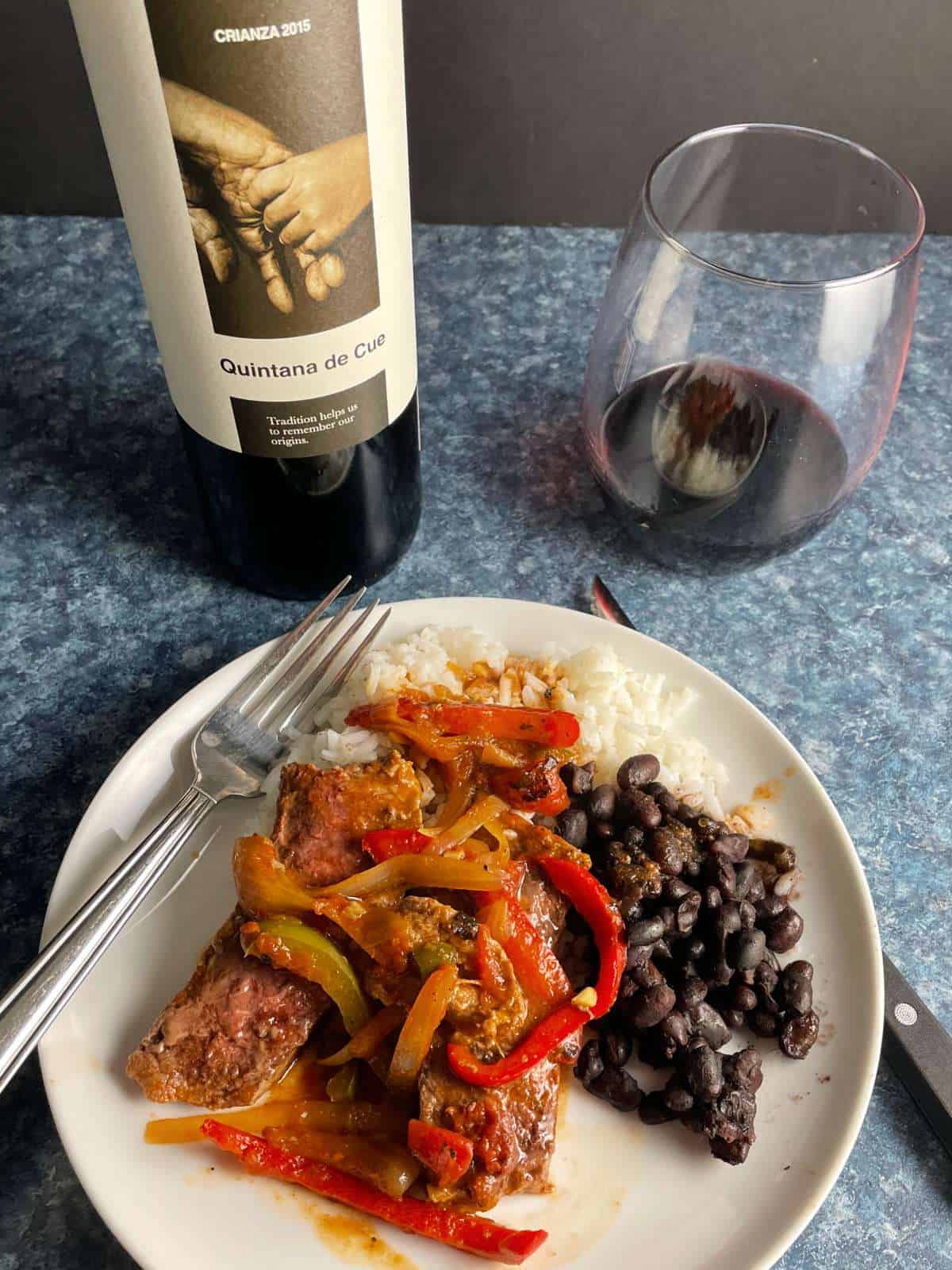 steak picado with black beans and rice on a white plate. Served with a red wine.