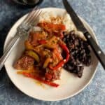 steak picado topped with onions and peppers. served on a white plate with black beans and rice.