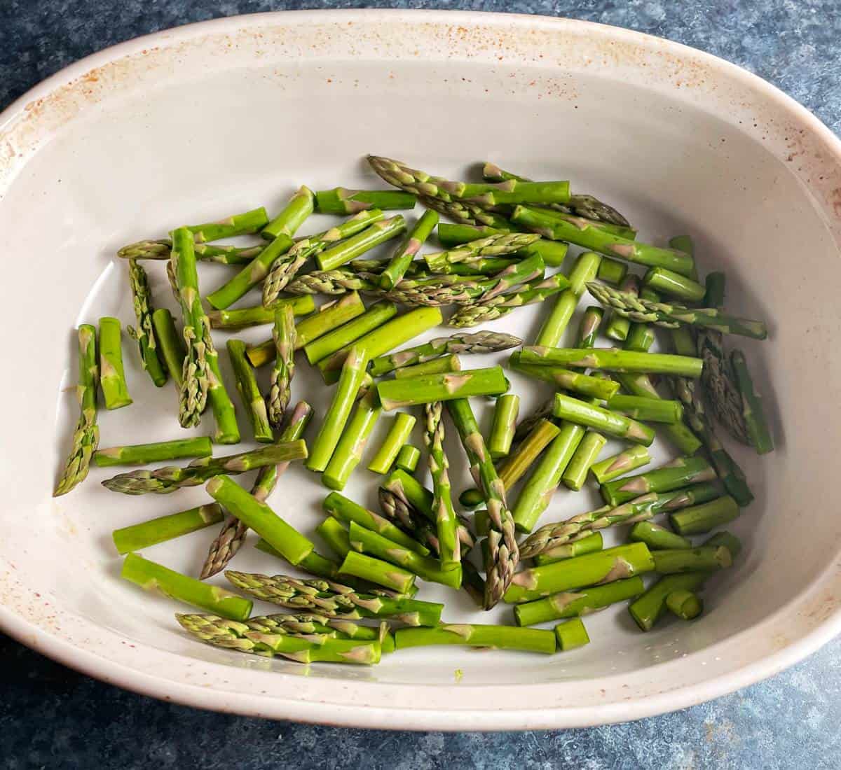 chopped asparagus arranged in a white baking dish.