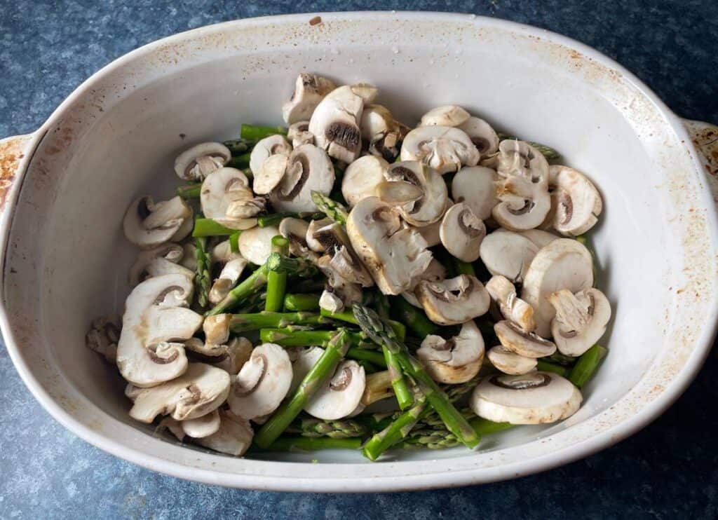 asparagus and sliced mushrooms arranged in a white baking dish. 