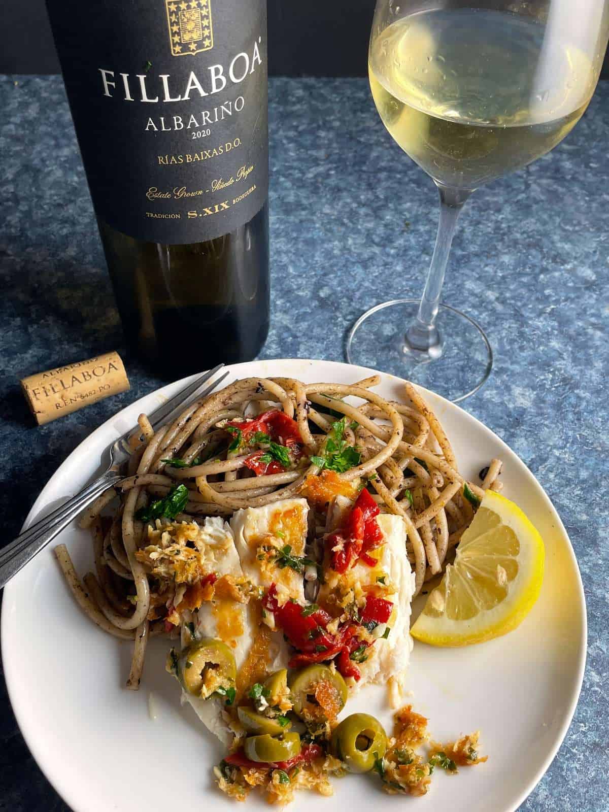 pan seared sea bass topped with olives and red peppers, served with spaghetti and a white wine.