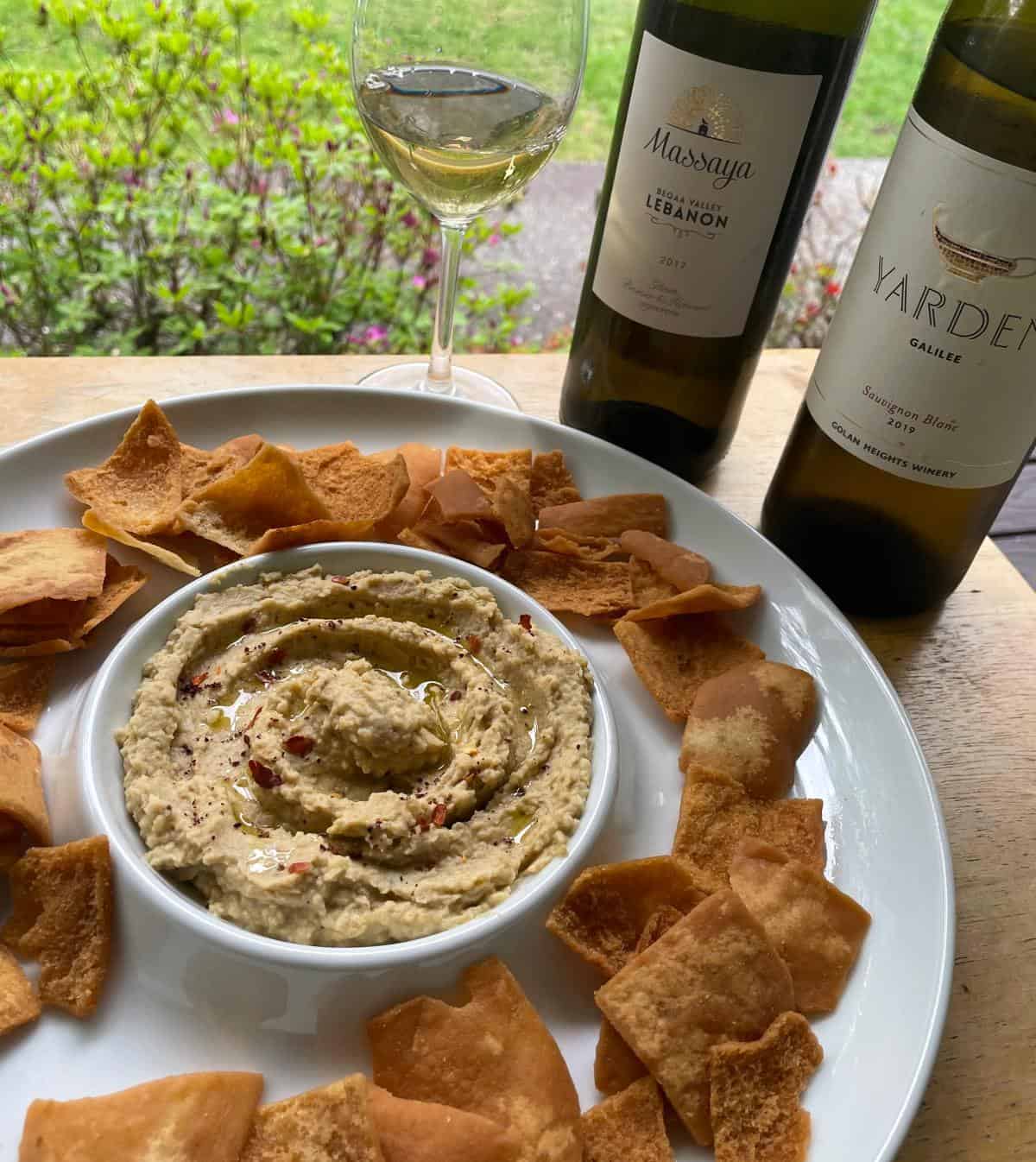 hummus in a white serving dish with pita chips, served with two bottles of white wine.