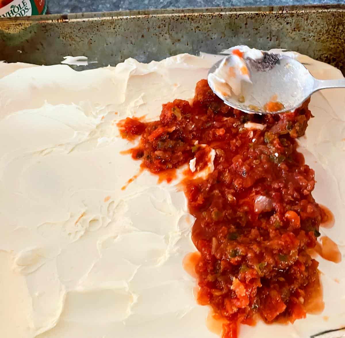 spreading a layer of salsa over some cream cheese in a baking dish.