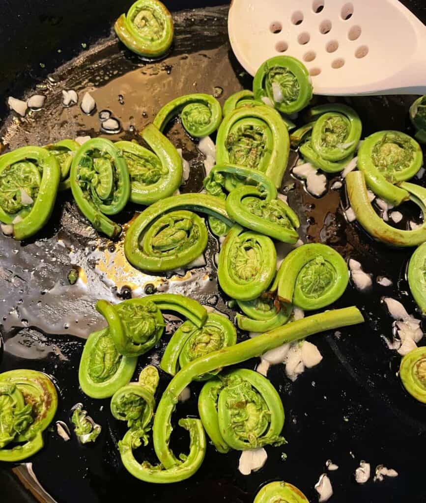 sautéing fiddlehead ferns in a skillet with garlic and olive oil.