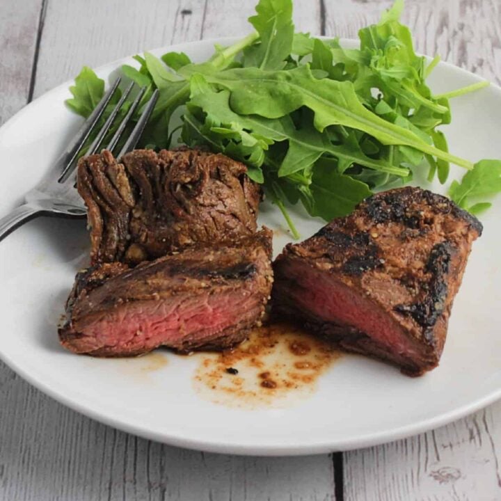 grilled steak tips on a white platter with a side of arugula greens.