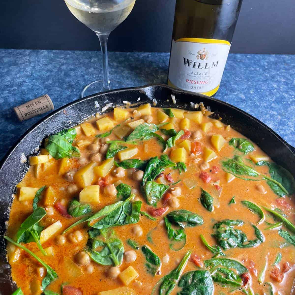 butternut squash chickpea curry with wilted spinach, in a black skillet.