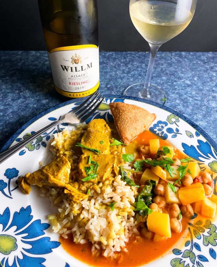 butternut squash chickpea curry plated with butter chicken and rice. Served with a Riesling white wine in the background.